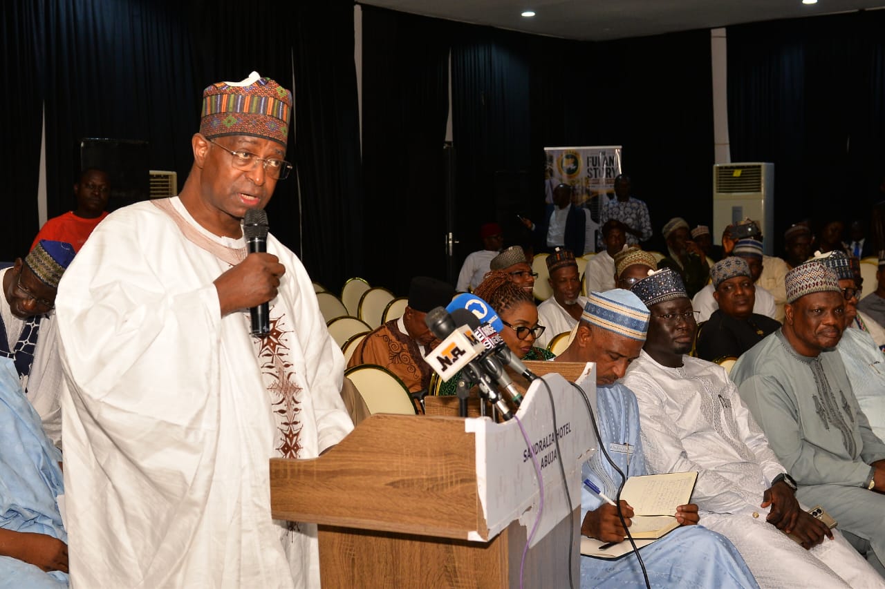 A speaker holding a microphone at a conference lectern beside seated attendees.